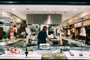 A chef prepares fresh seafood for sale at an indoor market, surrounded by ingredients and displays.