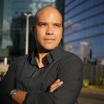 Portrait of a confident man outdoors against a modern glass building in bright daylight.